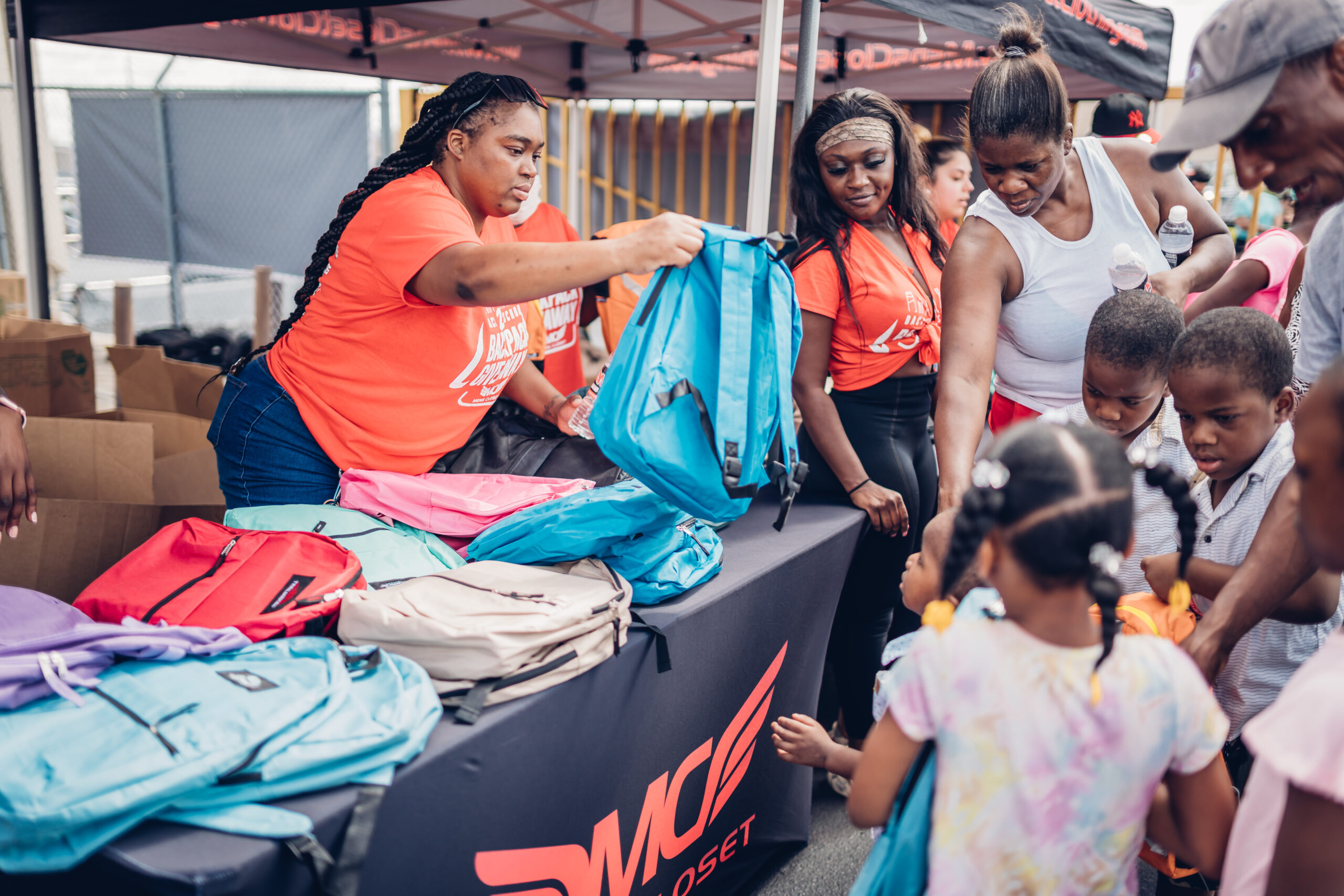 Volunteers from MC Community Care distribute colorful backpacks to children during a back-to-school giveaway event.
